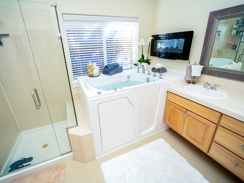 The image shows a bathroom interior with a large mirror above a sink, a bathtub, a walk-in shower, and a toilet.