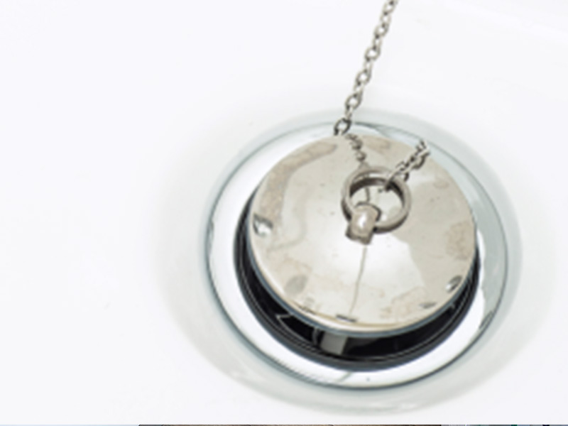 A silver pendant with a moon-like design hanging from a chain, set against a reflective surface.