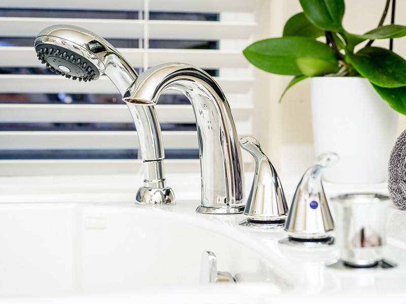 A chrome kitchen faucet with a sprayer, set against a white countertop.