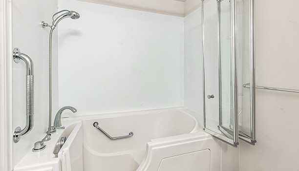 The image shows a bathroom interior with a white bathtub, a large mirror above the sink, and a shower enclosure with a glass door.