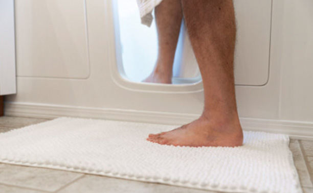 A person s feet are seen through an open washing machine door, with the rest of their body hidden from view.